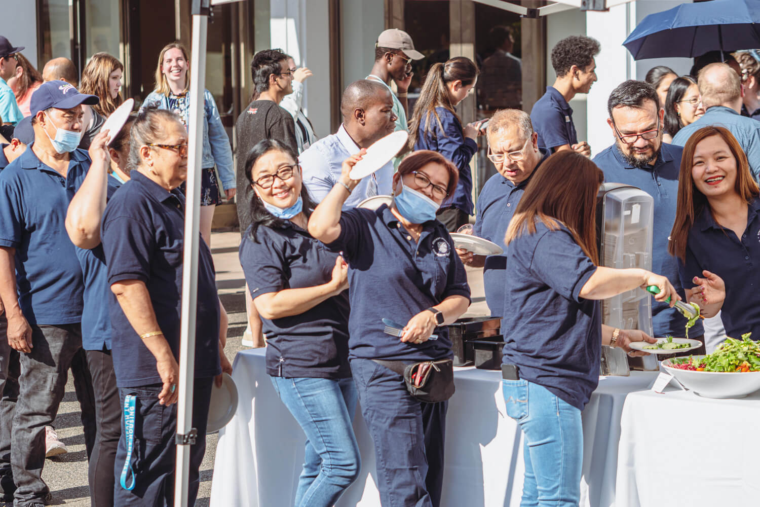A group of SHCS staff wearing navy blue SHCS shirts in line for food at the 2022 SHCS Staff Appreciation BBQ